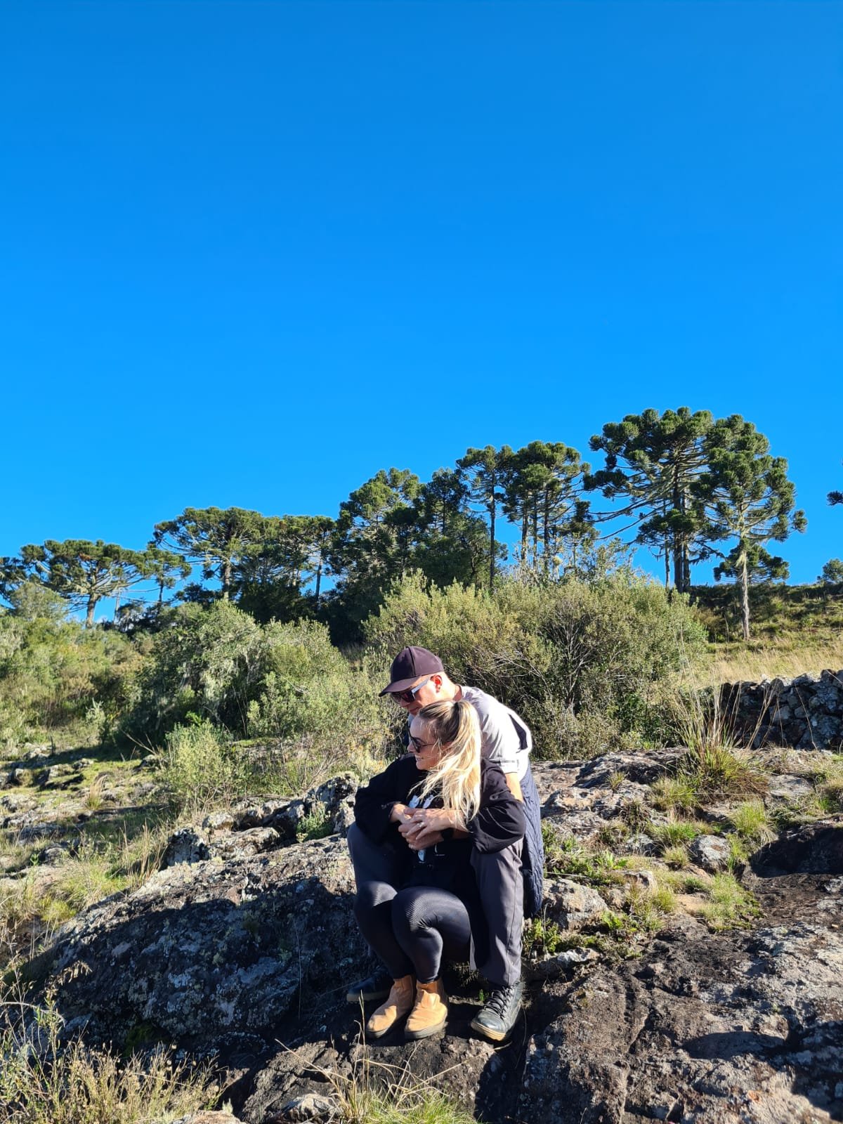 Casal nas araucárias sob o céu azul
